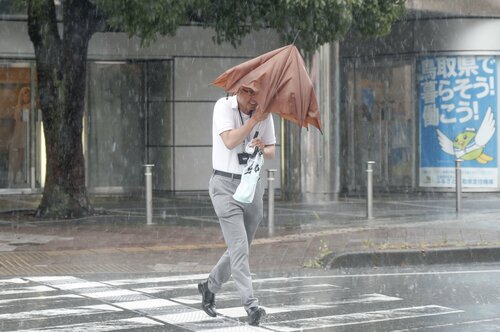 台風７号が接近し大雨と強風の中、傘を手に歩く人＝１５日午後０時３５分、ＪＲ鳥取駅前