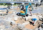 浴槽に流れ込んだ土砂や岩を重機などでかき出す作業員＝２４日、三朝町三朝の河原風呂