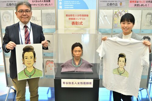 自身のイラストがプリントされたシャツを持つ渡部さん（右）＝９日、鳥取市青谷町吉川の青谷かみじち史跡公園