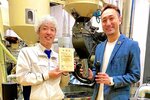日南町から贈られた木製の感謝状を掲げる萩原社長（左）