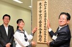 実行委の看板を掲げる（左から）伊木市長、松本さん、浦林教育長