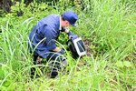 草むらに投棄されたプリンターを確認する市職員