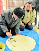 講元の山中正則さん（右）に見守られ、奉納する大餅に願い事を墨書きする孫の那斗さん