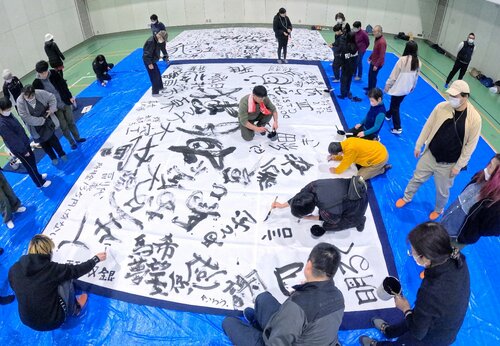 巨大な紙をさまざまな文字で埋め尽くす参加者