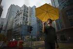 　大雨が降る香港の街角で、雨傘運動の象徴となった黄色い傘をさす周冠威。摩天楼の隙間から見える空には分厚い雲が広がっていた＝２０２４年９月、香港（撮影・武隈周防、共同）