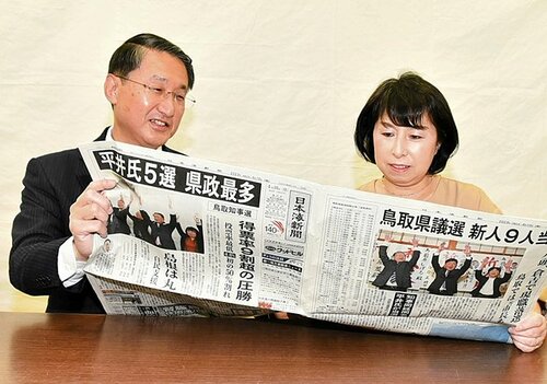 自身が果たした県政初の５選を報じる本紙に目を通す平井氏（左）とりえ夫人＝１０日、鳥取市新町の選挙事務所
