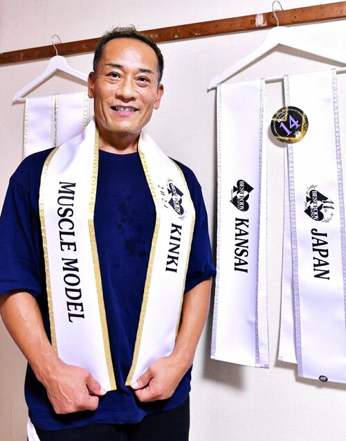 優勝者に贈られる金色に縁取られたサッシュを手にする井藤さん